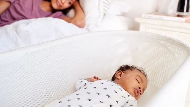 New mom watching infant sleep in a bassinet