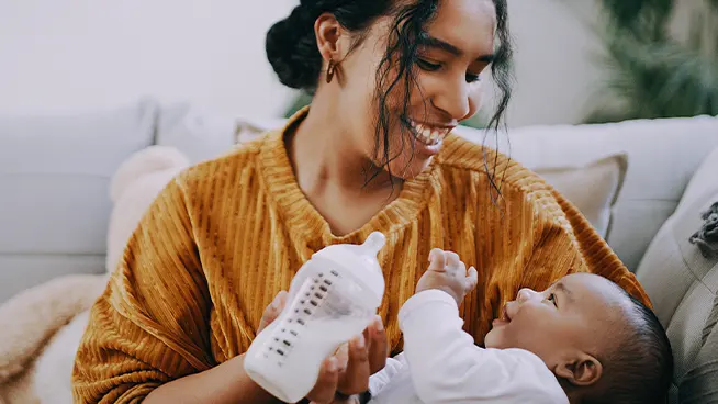 Mamá sonriendo al bebé mientras sostiene un biberón