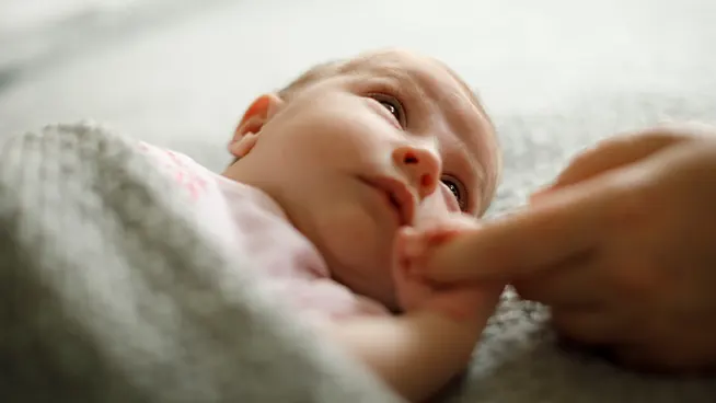 Newborn holding mom's finger while looking at her