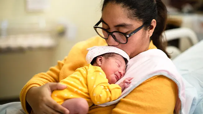 Madre sosteniendo tiernamente al bebé sobre su pecho, besando al bebé en la cabeza