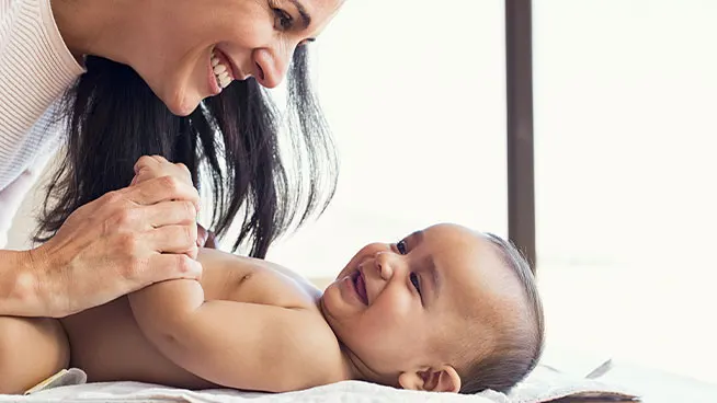 Madre sonriente apoyada en su bebé feliz, sosteniendo el brazo de su bebé