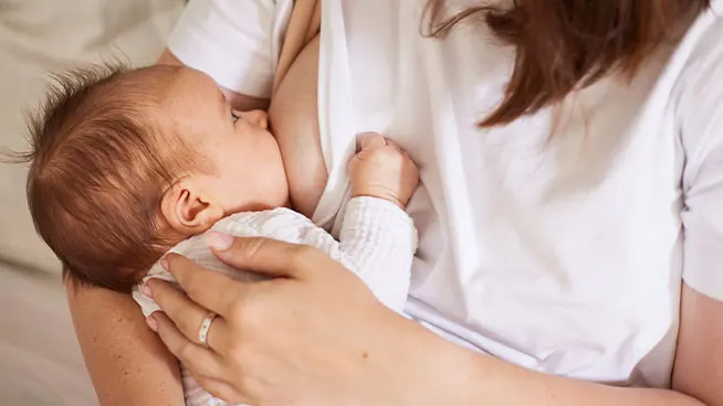 Baby breastfeeding as mom holds baby closely