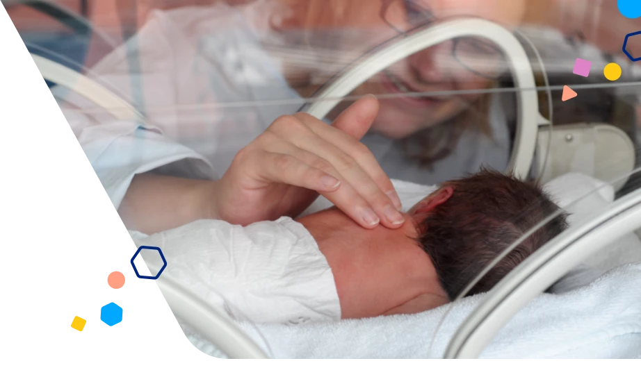 Baby laying in a bed in the NICU with a parent touching their back