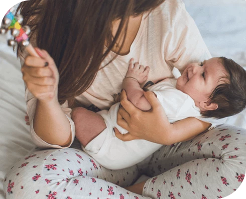 Bebé sonriente sostenido por mamá que agita un sonajero colorido