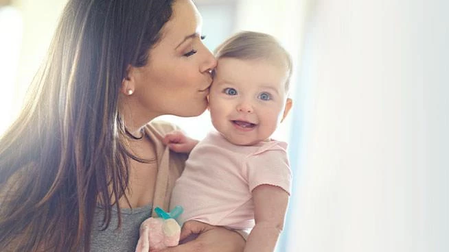 Mom holding her smiling daughter and kissing her on the cheek