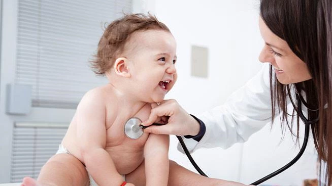 Doctor holding stethoscope to smiling babys chest