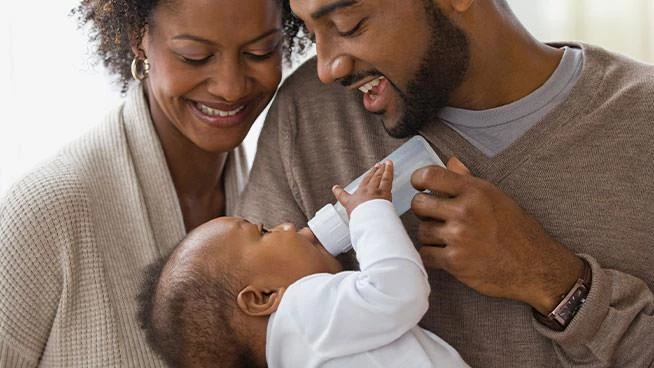 Mamá y papá felices alimentando a su bebé con un biberón