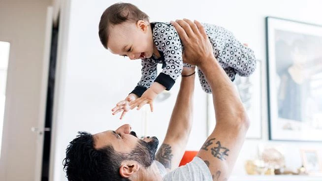 Papá sonriente levantando a su bebé feliz en el aire