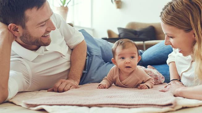 Dad and mom laying on the floor with 5 month old baby during tummy time