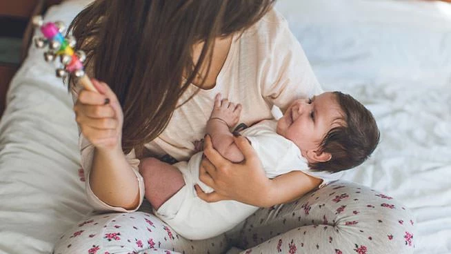 Mom holding baby bell toy above infant baby