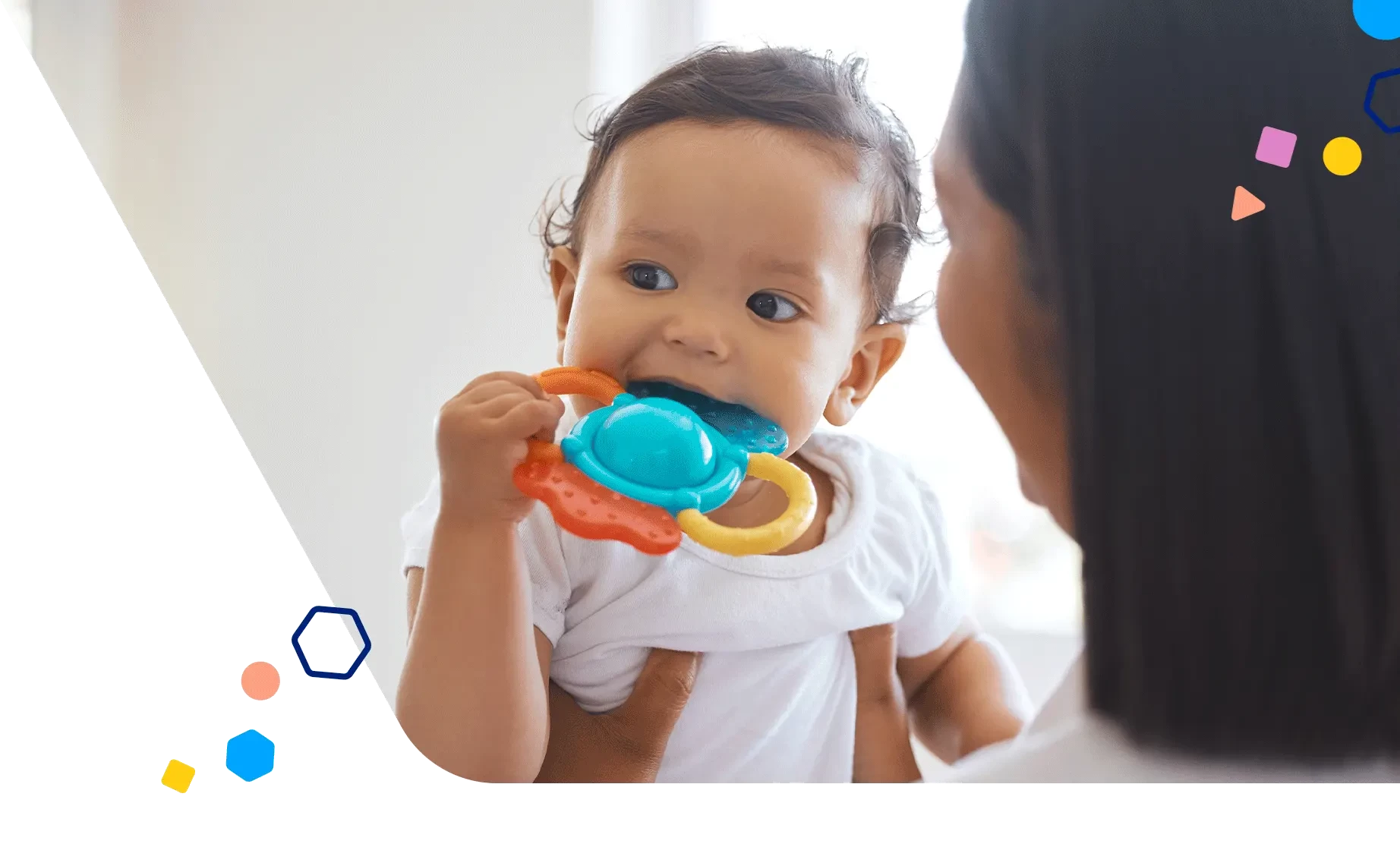 Madre sosteniendo a un bebé al que le están saliendo los dientes en un juguete colorido