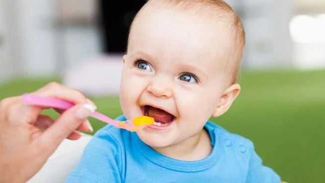 Baby smiling while mom spoon-feeds her