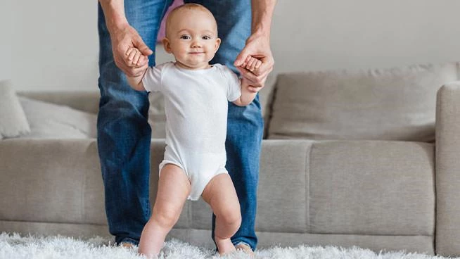 Dad holding baby's hands as they learn to walk