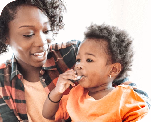 Toddler happily eating food while smiling mom holds them