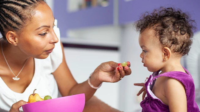 Mom giving a grape to toddler daughter