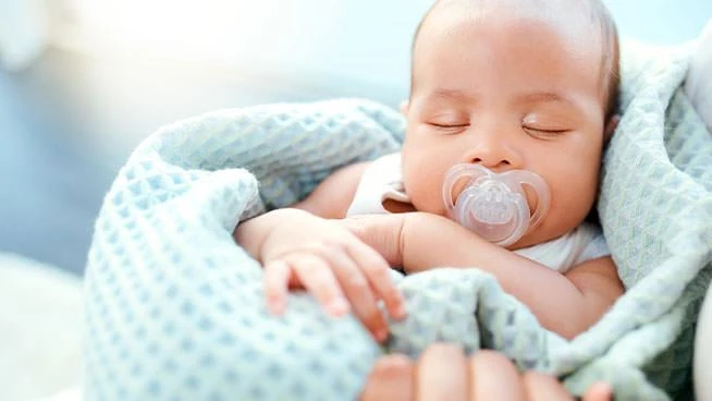 Baby wrapped in blue blanket sleeping in parent's arms