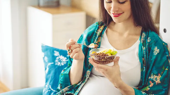 Mujer embarazada sosteniendo una cuchara y un plato de comida sana