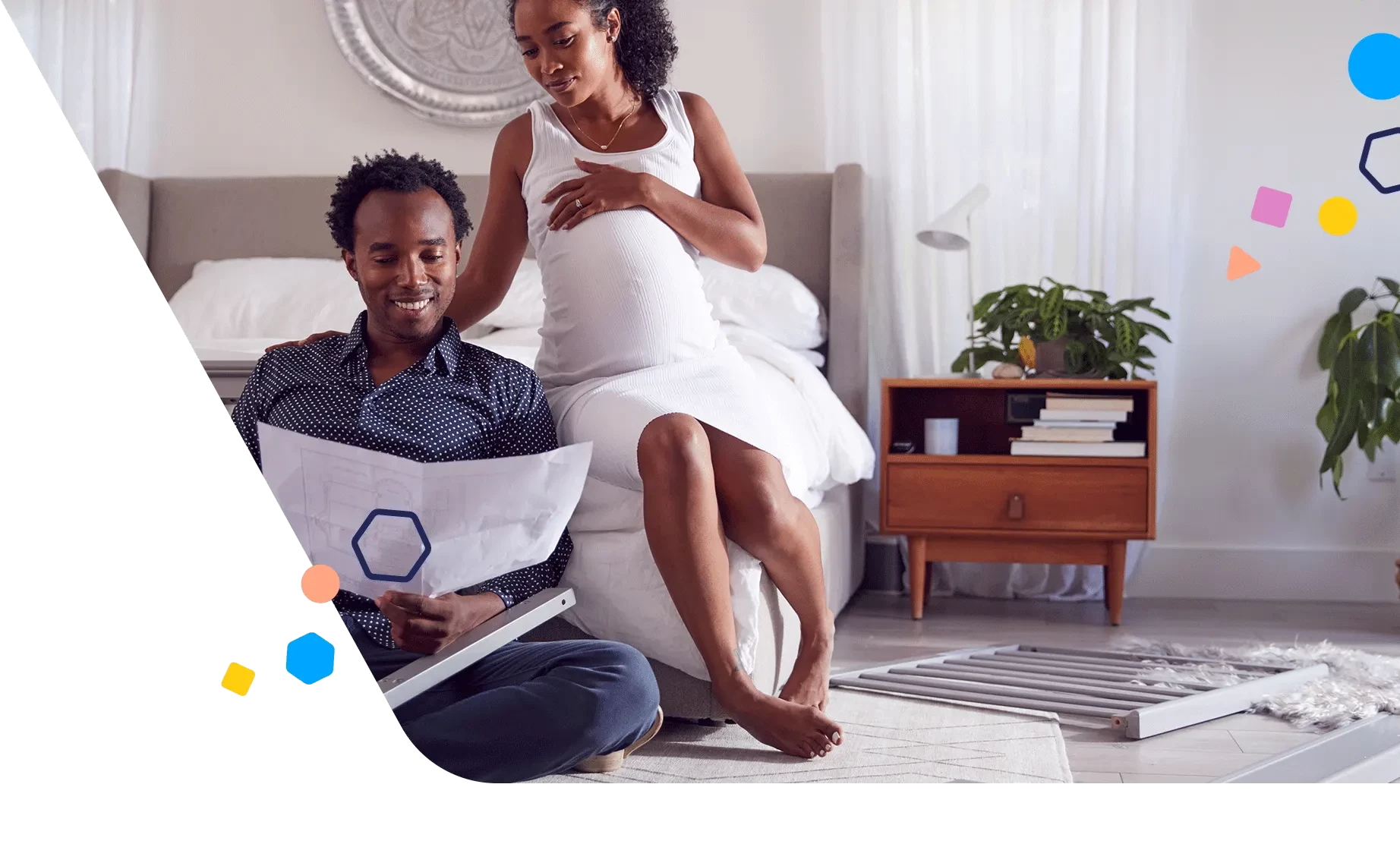 Pregnant woman sitting on the edge of the bed as her spouse looks at instructions for putting a crib together