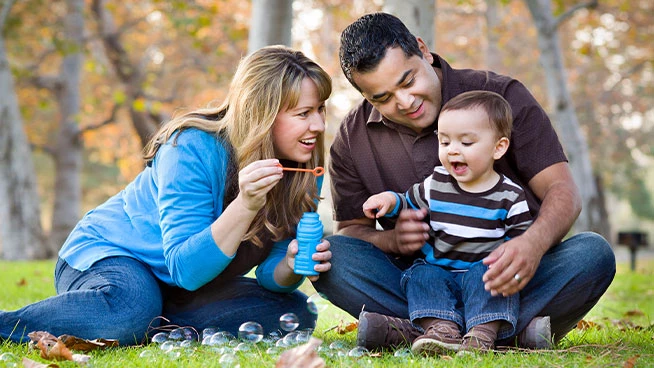 Mamá y papá haciendo burbujas afuera en el césped con su bebé