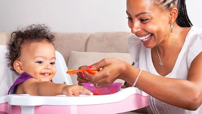 Baby in a high chair being spoon-fed by mom