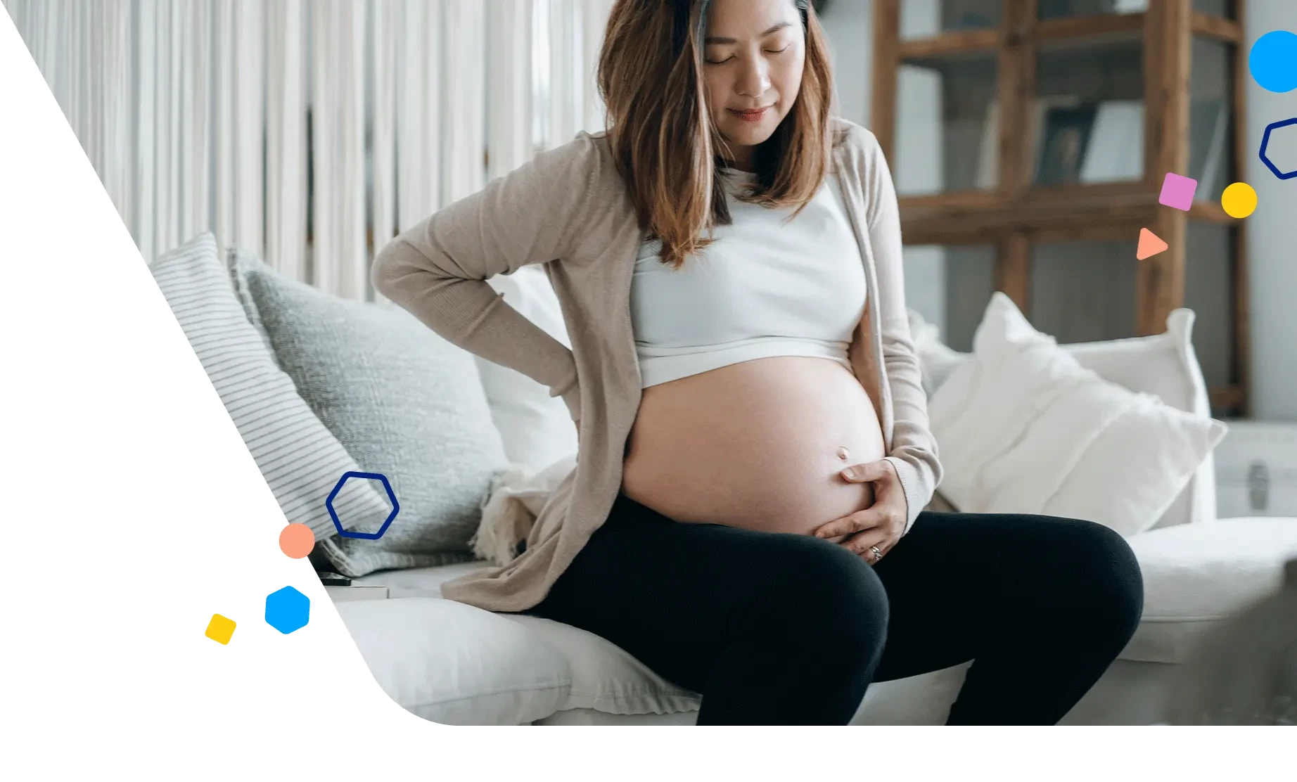 Pregnant woman sitting on the couch holding her belly bump and back