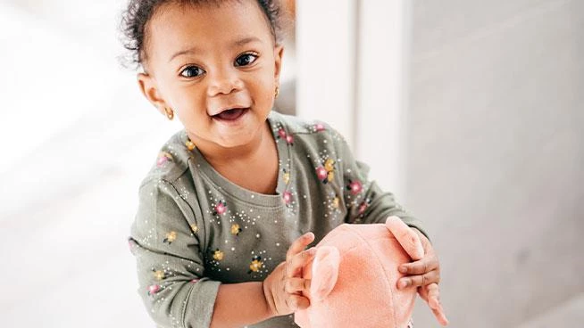 Toddler girl holding pink stuffed animal and smiling