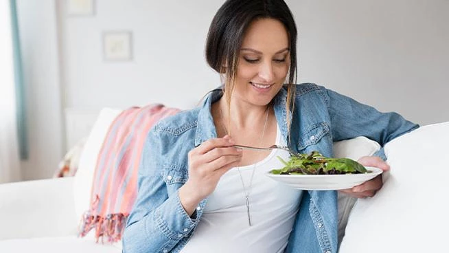 Mamá embarazada comiendo una ensalada de hojas verdes