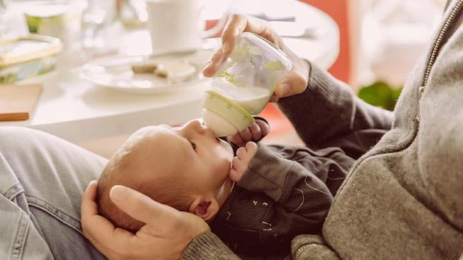 Parent sitting down and bottle feeding their baby