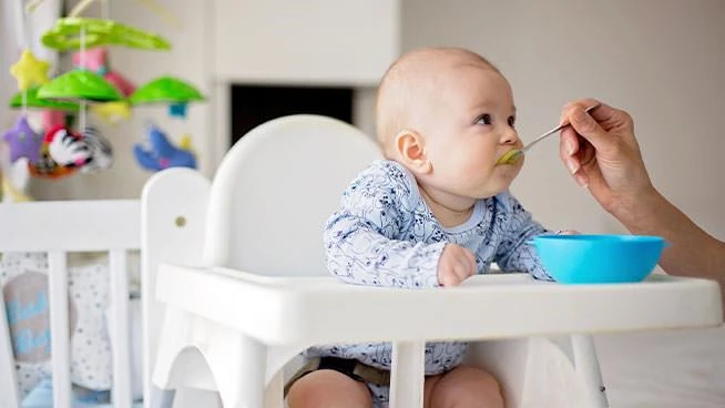 Baby eating baby food while sitting in a high chair