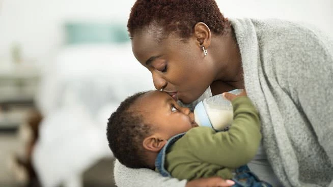 Mom kissing baby on the forehead as baby drinks from a bottle