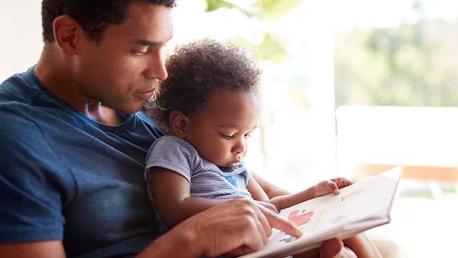 Dad holding his toddler both reading a book