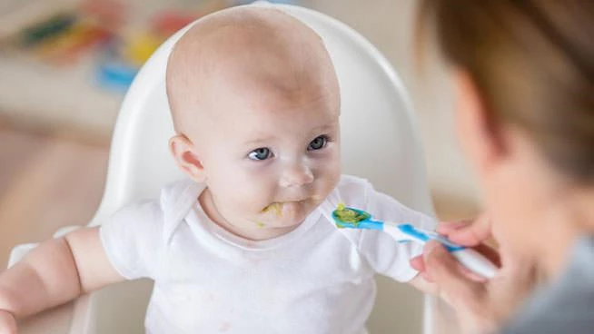 Mom spoon feeding infant in a high chair