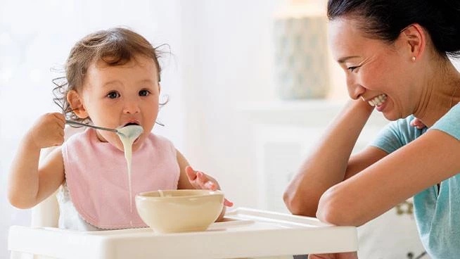 Mom laughing as toddler tries to feed herself