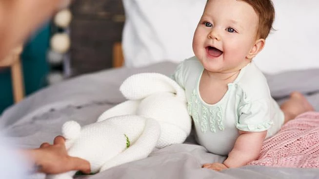 Niña tirada en el suelo con un animal de peluche mirando a su mamá