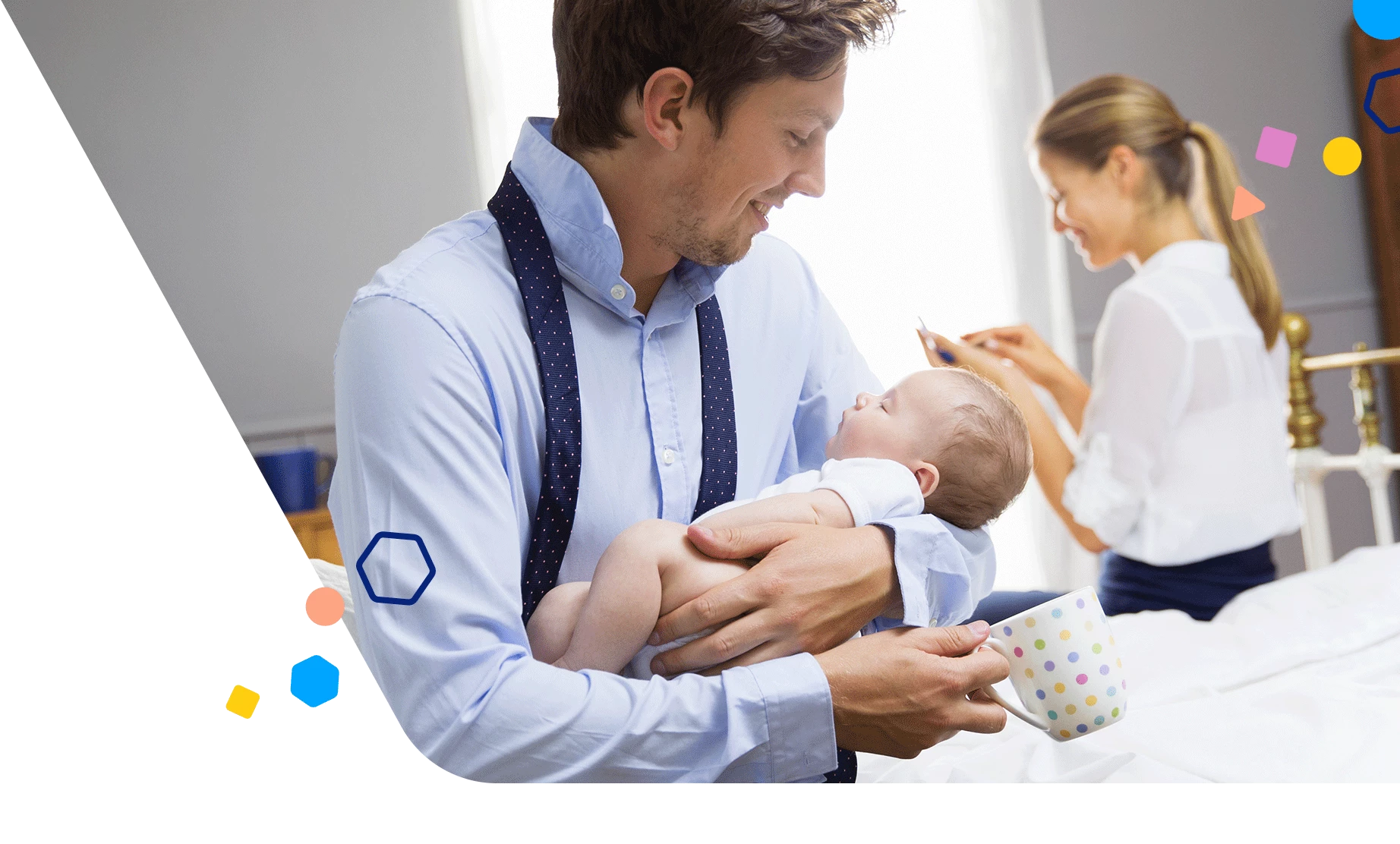 Dad holding his baby as mom gets ready for work in the background