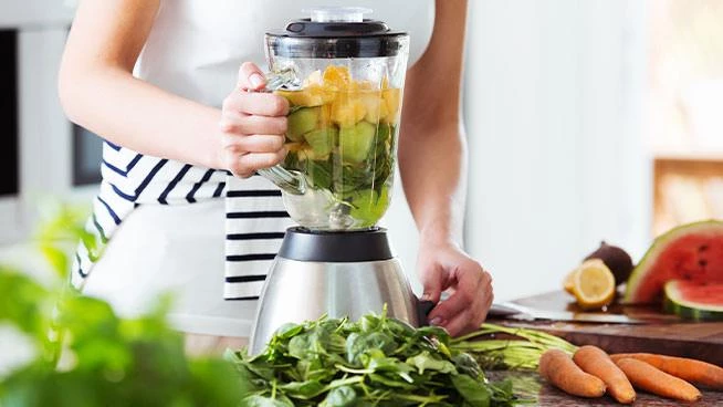 Woman putting vegetables in a blender