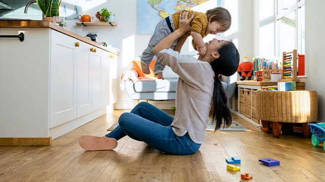 Mom smiling and holding toddler up in the air while they play