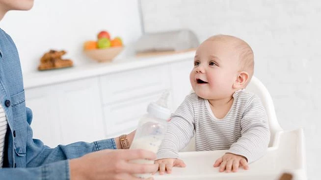 Baby in a high chair getting a bottle from mom