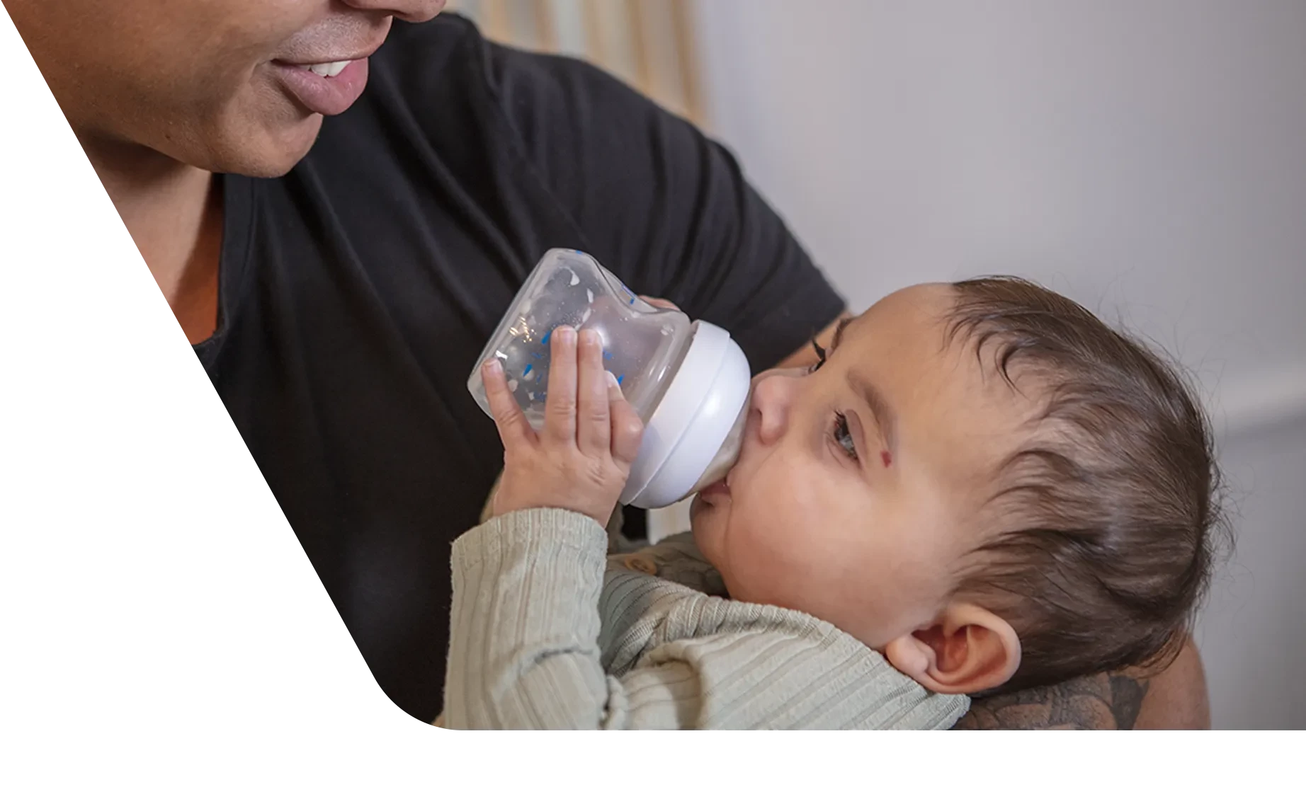 Dad smiling at his baby as the baby holds their own bottle