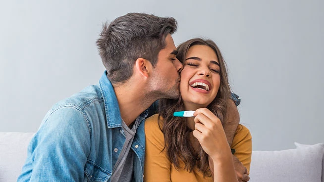 Husband kissing wife who's holding up a pregnancy test