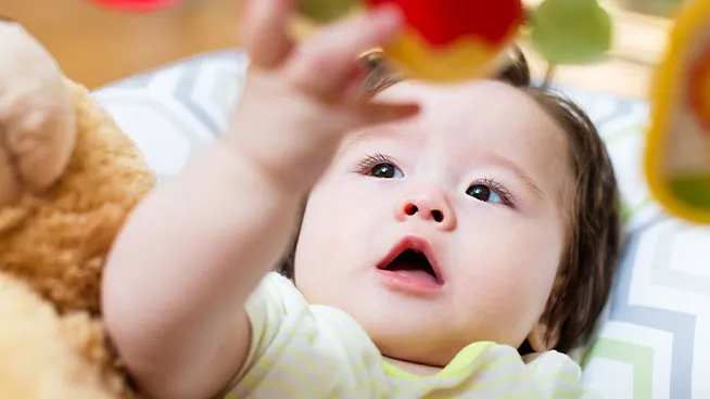 baby playing with toy while lying on a play mat