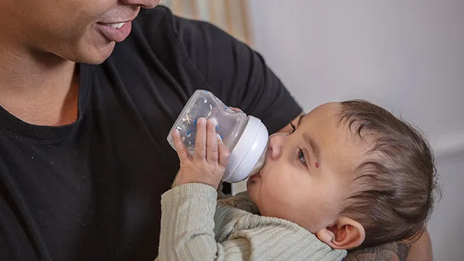 Dad smiling at his baby as the baby holds their own bottle