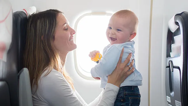 Smiling mother holding happy baby in an airplane seat.